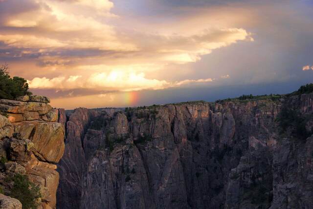A rainbow glowing faintly against a dramatic sunset sky over the sheer cliffs of the Black Canyon