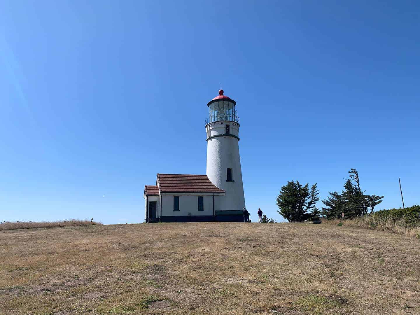Cape Blanco Lighthouse and its attached keeper's quarters on a grassy bluff under clear blue sky