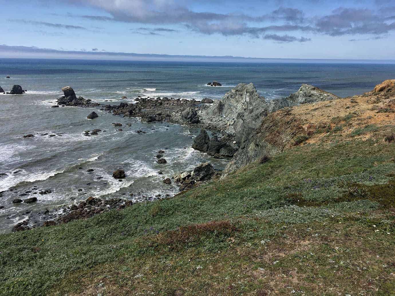 A steep green-gray rock point jutting into the ocean, with a long sandy beach and coastline stretching into the distance