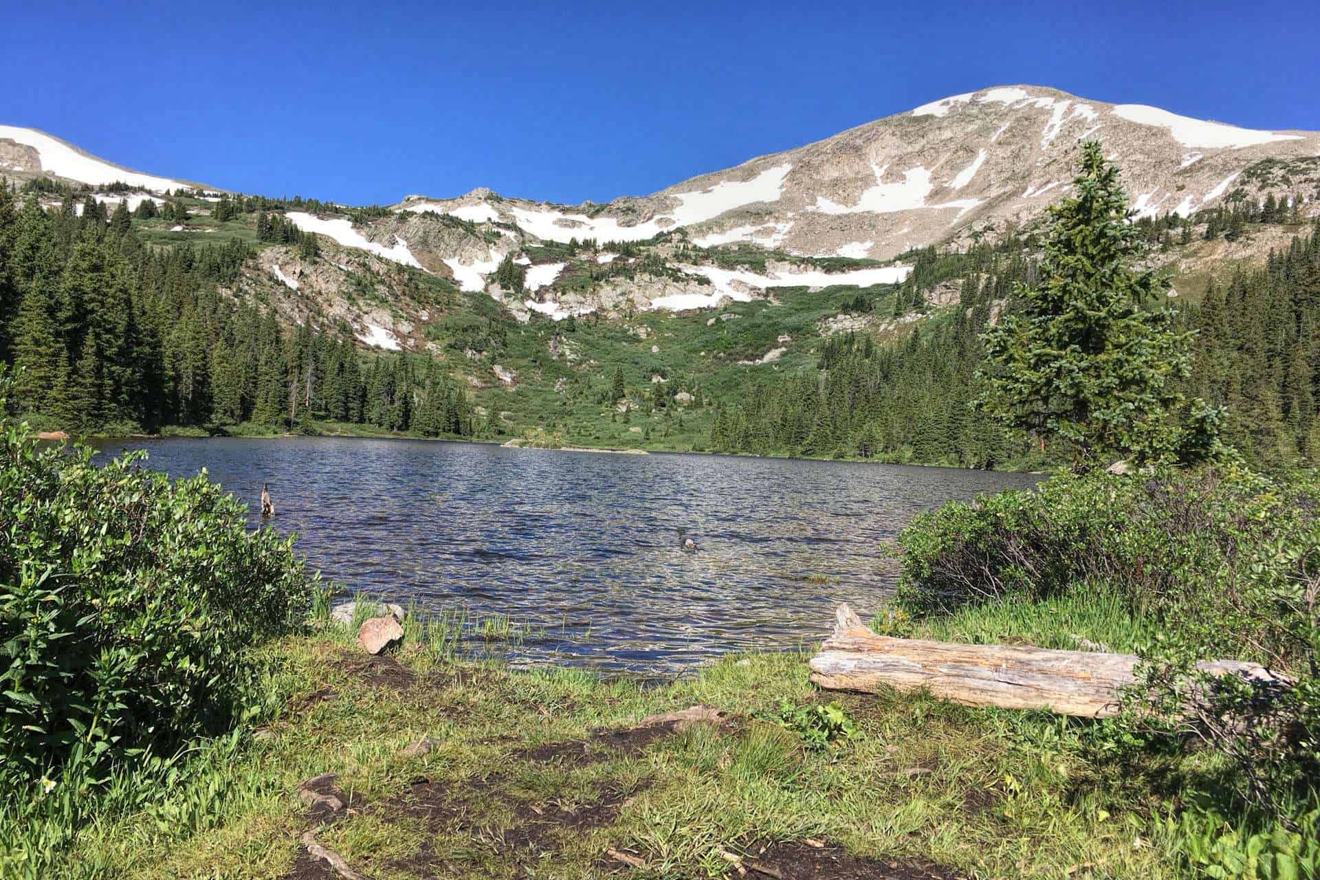 Kroenke Lake reflecting a snow-streaked mountain ridge under a clear blue sky