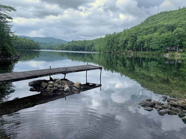 A wooden dock reaching into a calm forested lake under a cloudy sky