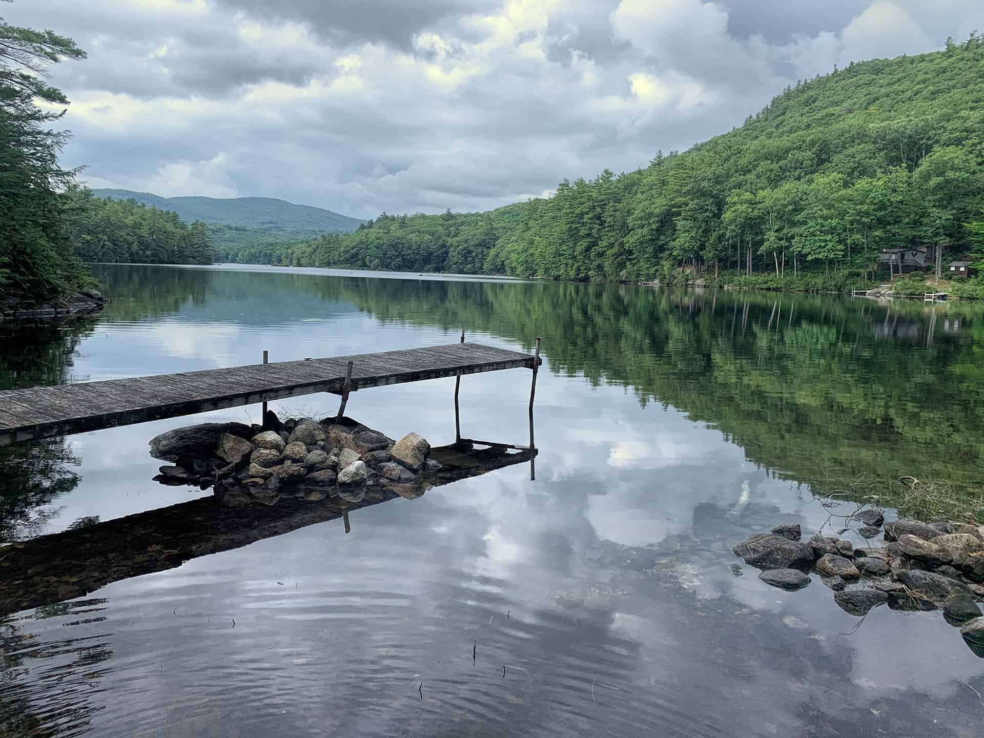 A wooden dock reaching into a calm forested lake under a cloudy sky